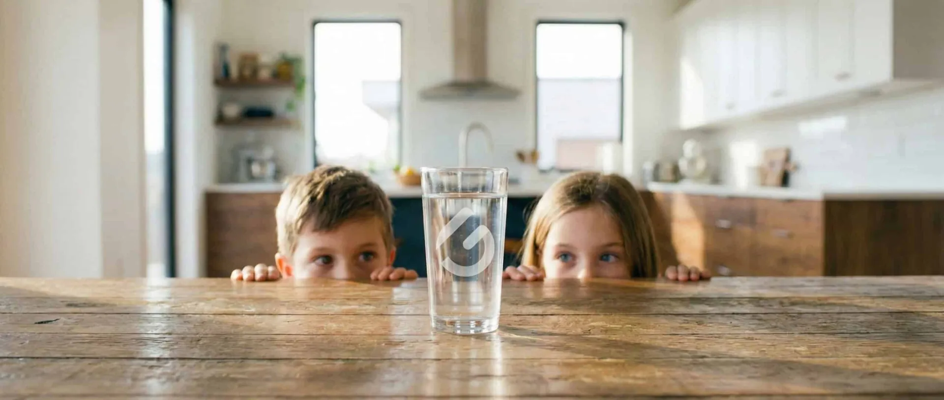 Zwei Kinder schauen über eine Tischkante auf ein Glas Wasser